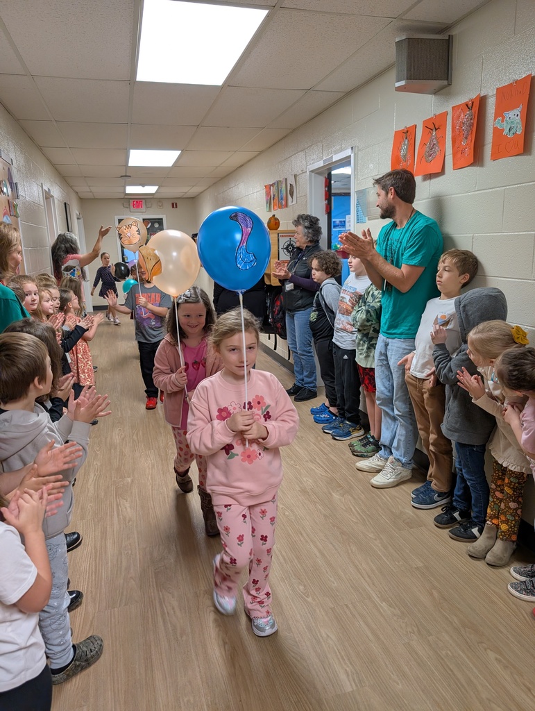 Group of kids walking in a school hallway holding balloons on sticks 