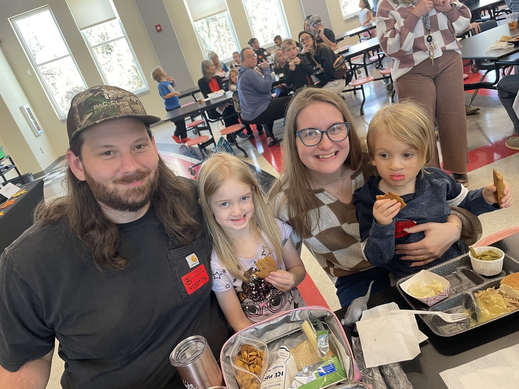 family sitting at a lunchroom table eating lunch posing and smiling 