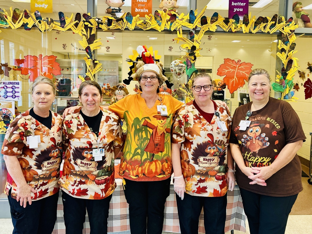 group of women standing closely side by side dressed in thanksgiving attire in a school cafeteria