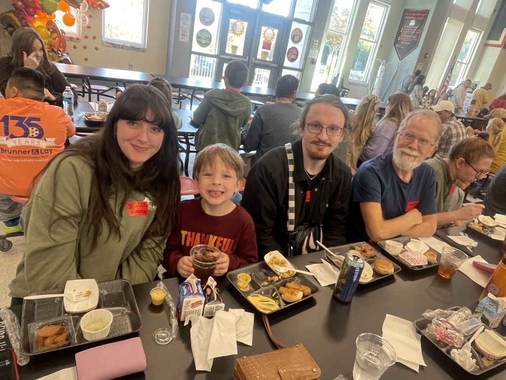 family sitting at a lunchroom table eating lunch posing and smiling 
