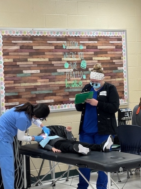 A student is receiving dental care at a PCSD school from 2 dental professionals.