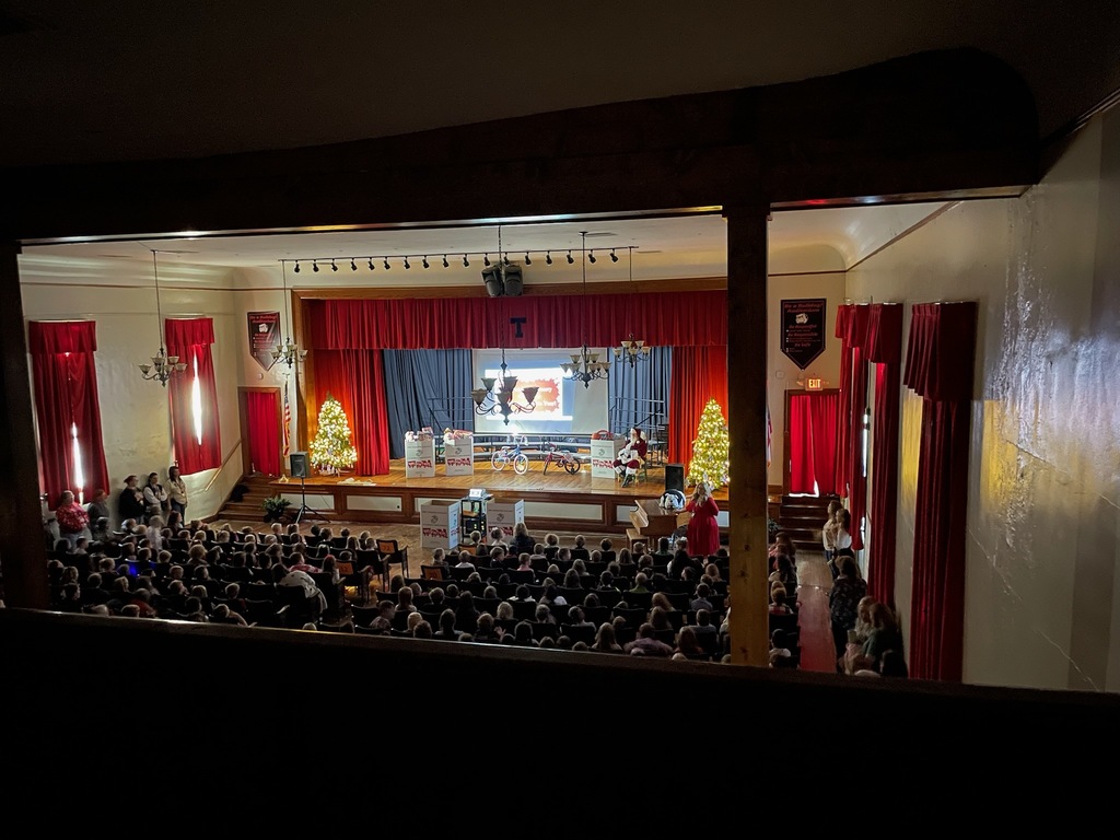 Auditorium filled with kids boxes on stage filled with toys, children holding candles
