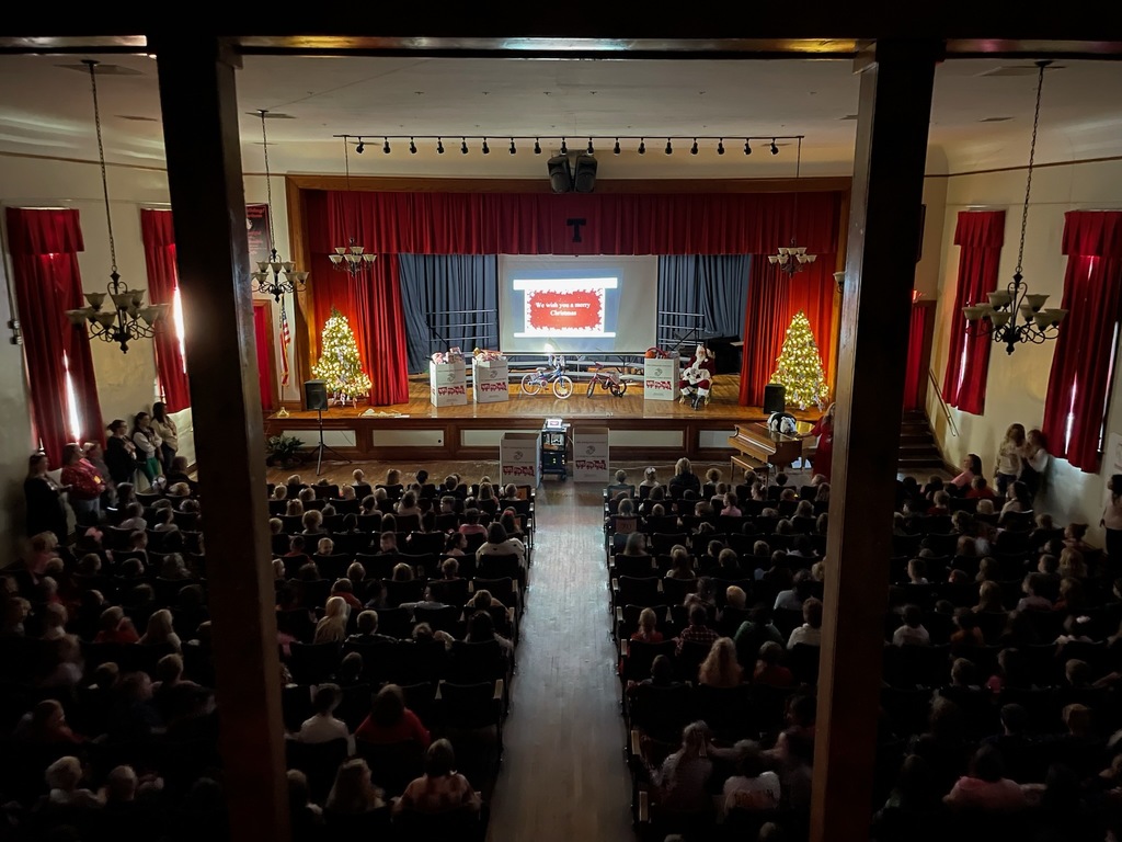 Auditorium filled with kids boxes on stage filled with toys, children holding candles