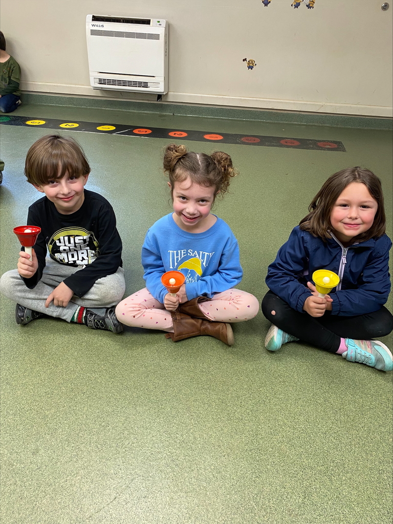 Three students holding bells sitting on the floor
