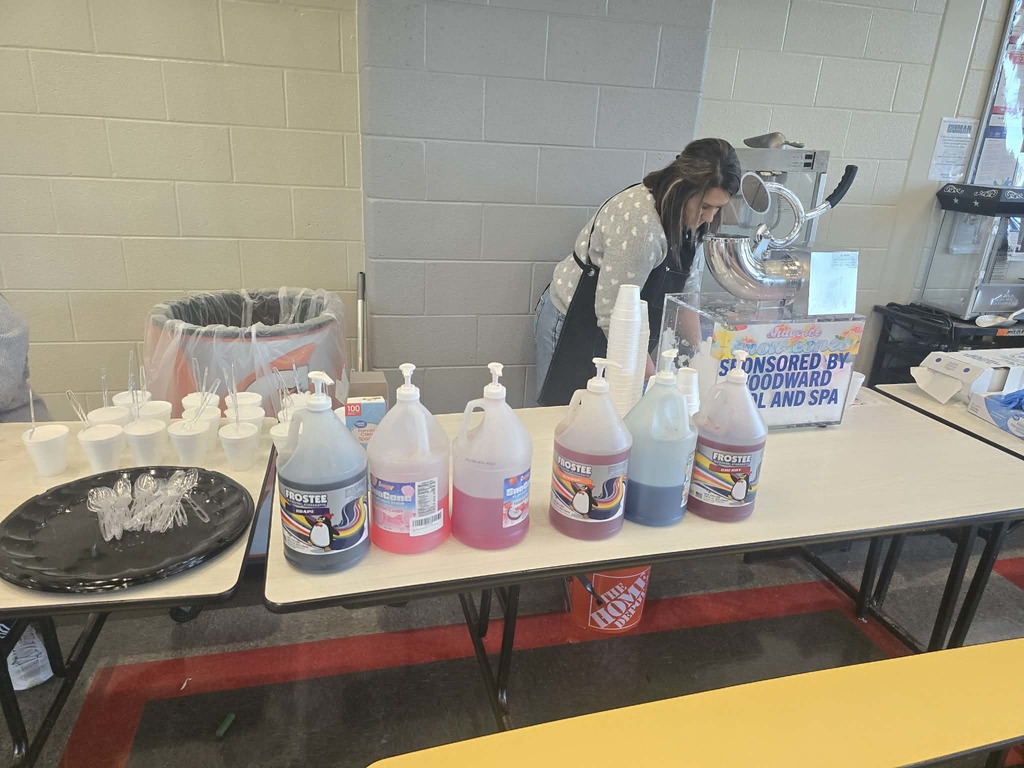 Metal snow cone maker with sponsor sign and women making snow cones