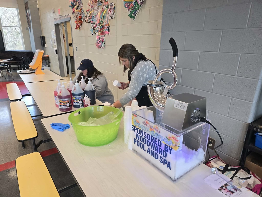 Metal snow cone maker with sponsor sign and two women making snow cones