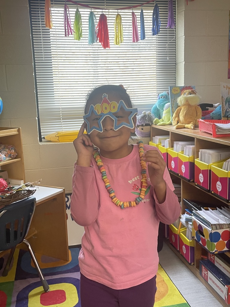 Female student wearing glasses with the #100 on it wearing a necklace made of fruit loops.