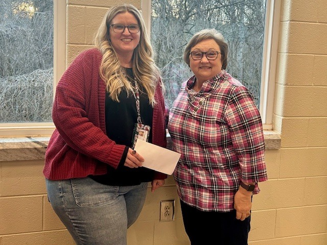 Two women standing in front of a window. One woman is holding a piece of paper.