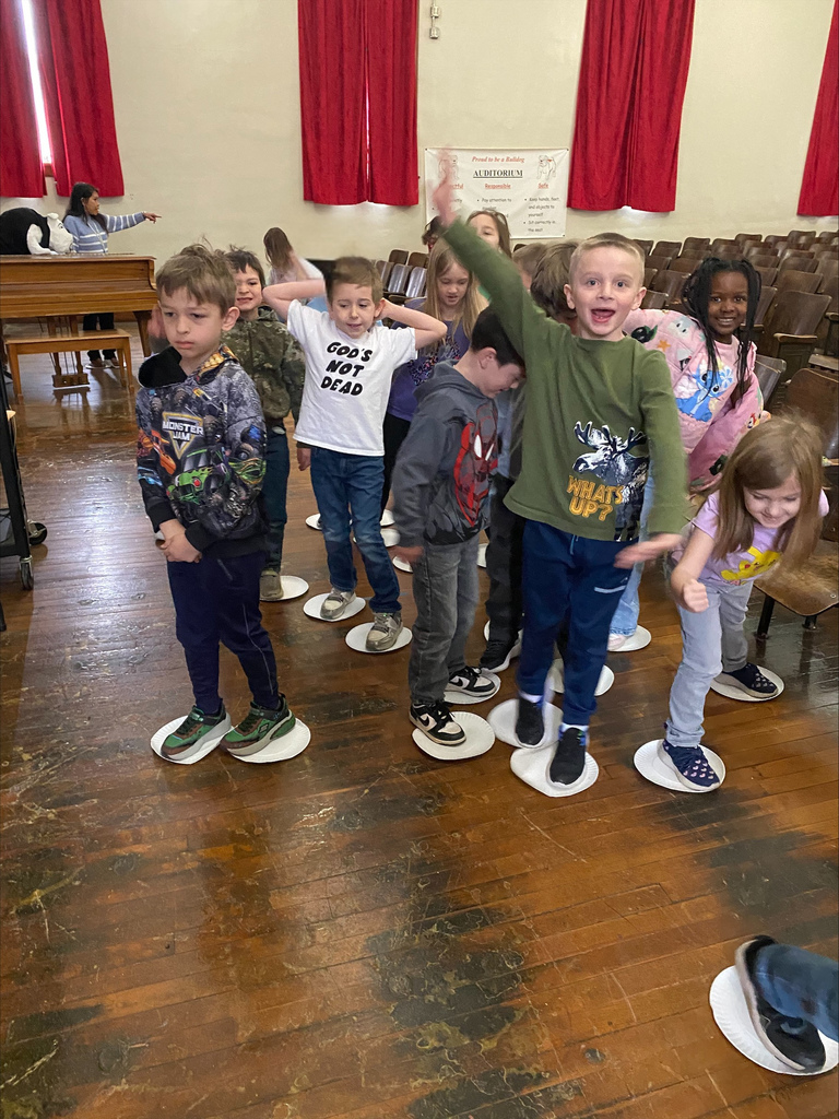 group of children standing on paper plates in a school auditorium