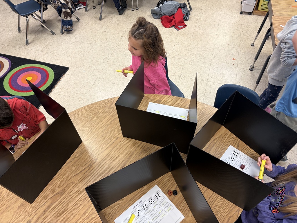 Young female student sitting at a table with other peers wearing a pink shirt and holding a yellow highlighter