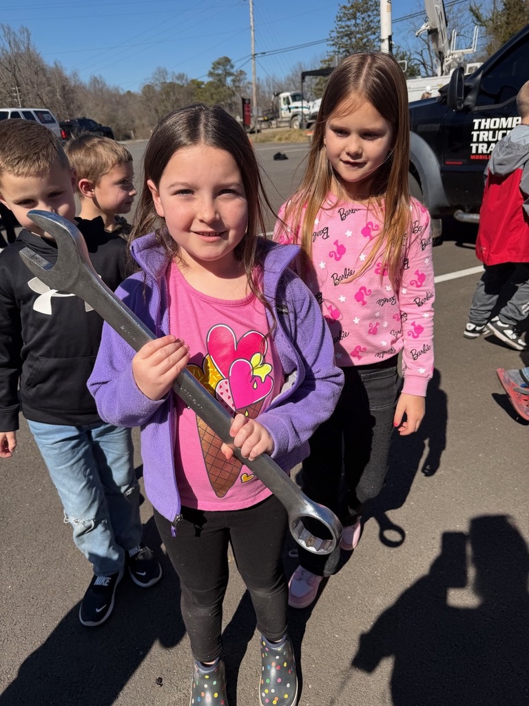 Two female students standing outside, one is holding a wrench