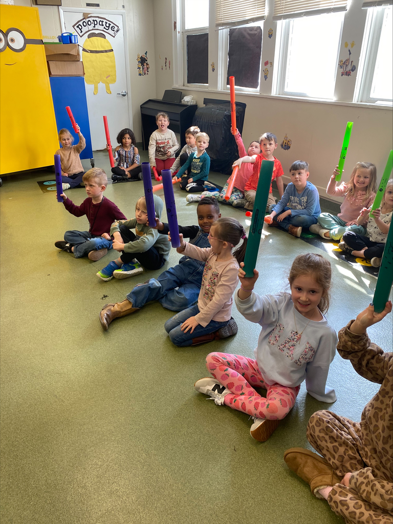 group of children sitting on the floor holding up musical instruments