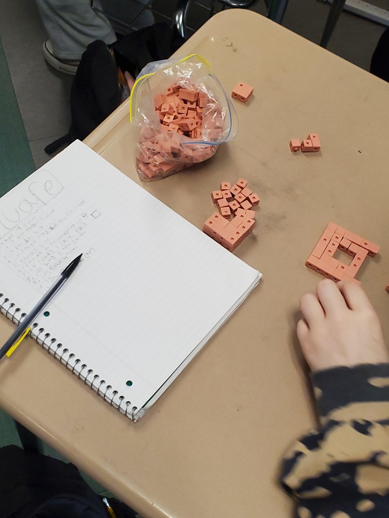 Student's desktop with a notebook, snap cubes and hand arranging the cubes