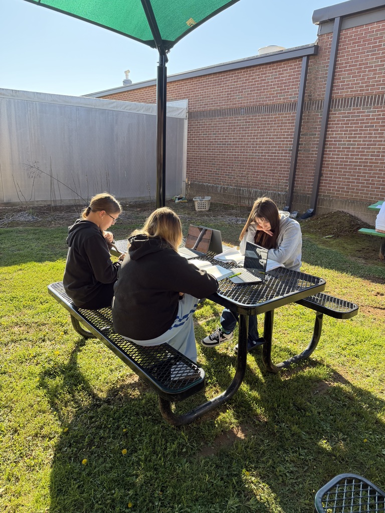 3 Students sitting at a picnic table and working on an assignment