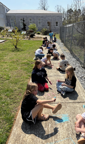 a row of students sitting on the sidewalk with sidewalk chalk