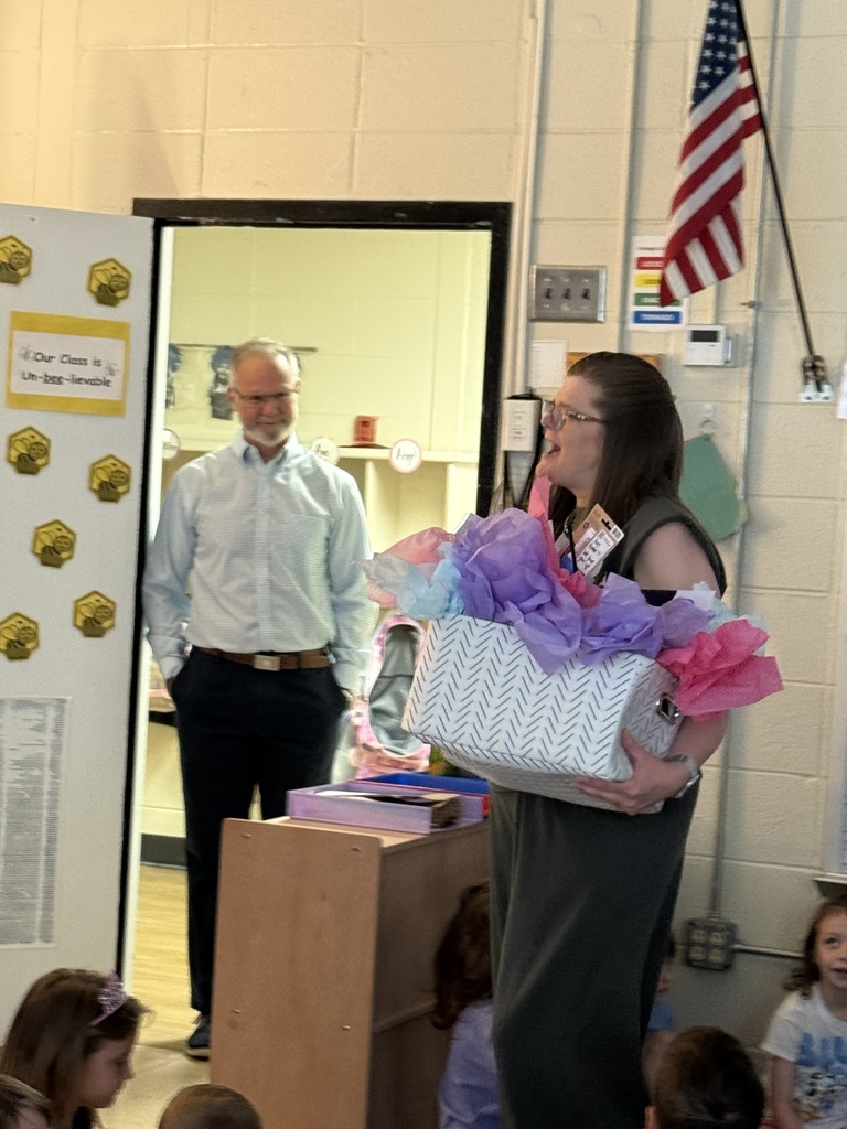 Woman holding a gift basket and a man standing in the doorway of a classroom
