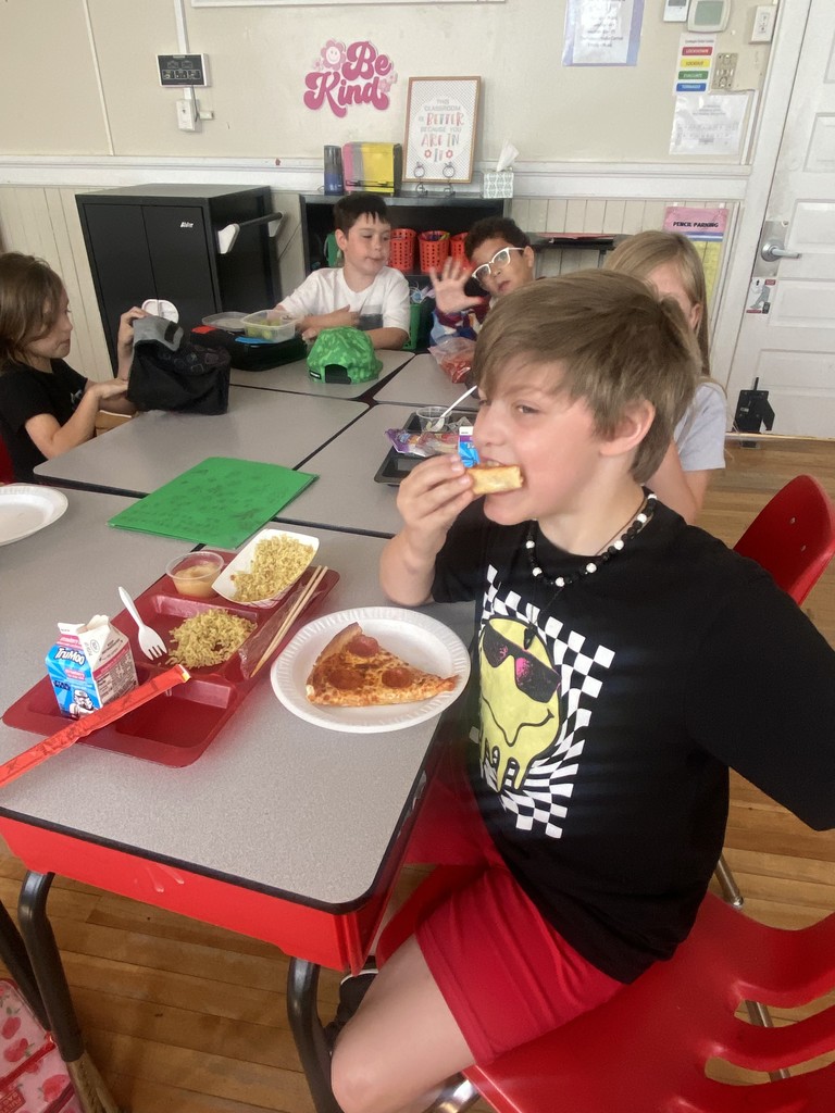 Children sitting at a group of tables eating pizza