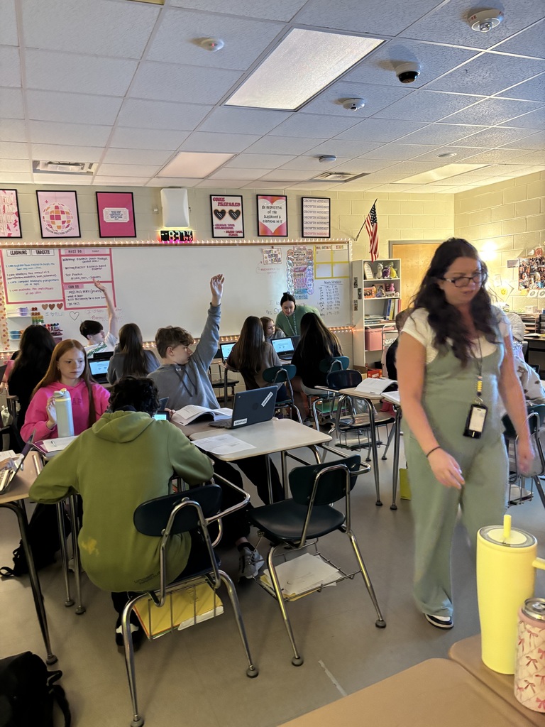 Students sitting at desks working. Mrs. Weaver is nearby to assist.