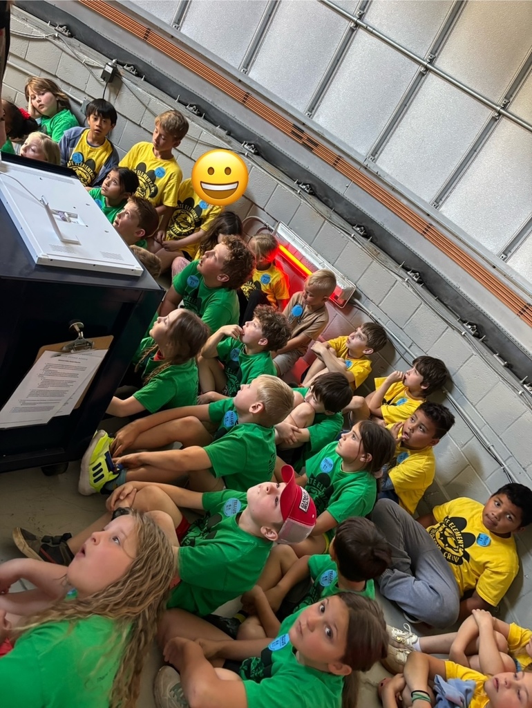 Large group of kids sitting in a semi circle some are wearing green shirts, some are wearing yellow shirts