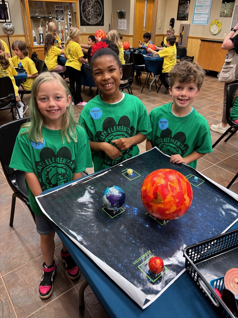 Three students in green shirts standing around a group of planets