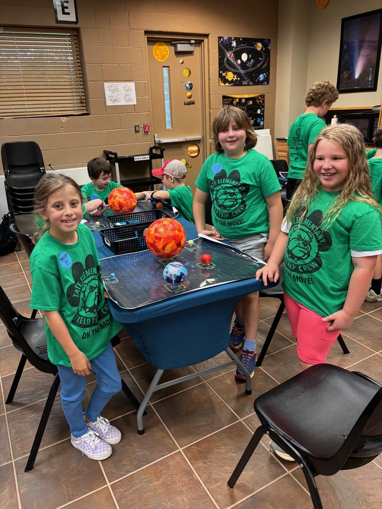 Three students in green shirts standing around a group of planets