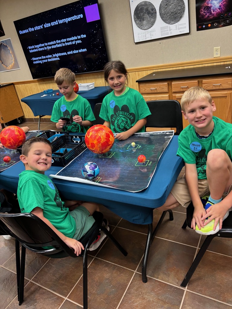 Three students in green shirts standing around a group of planets