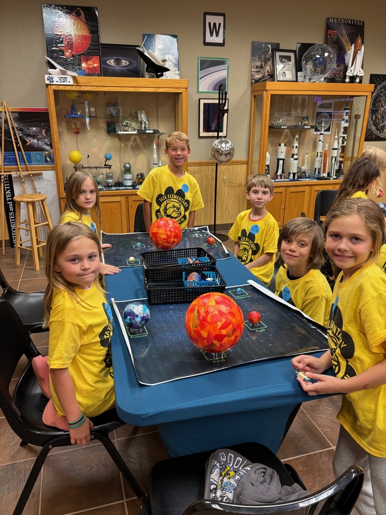 Group of students in yellow shirts standing around a group of planets