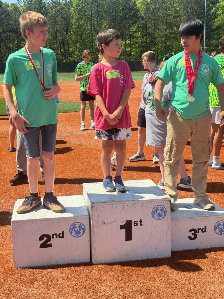 Three kids standing on a podium. Two are wearing green,  one is wearing pink