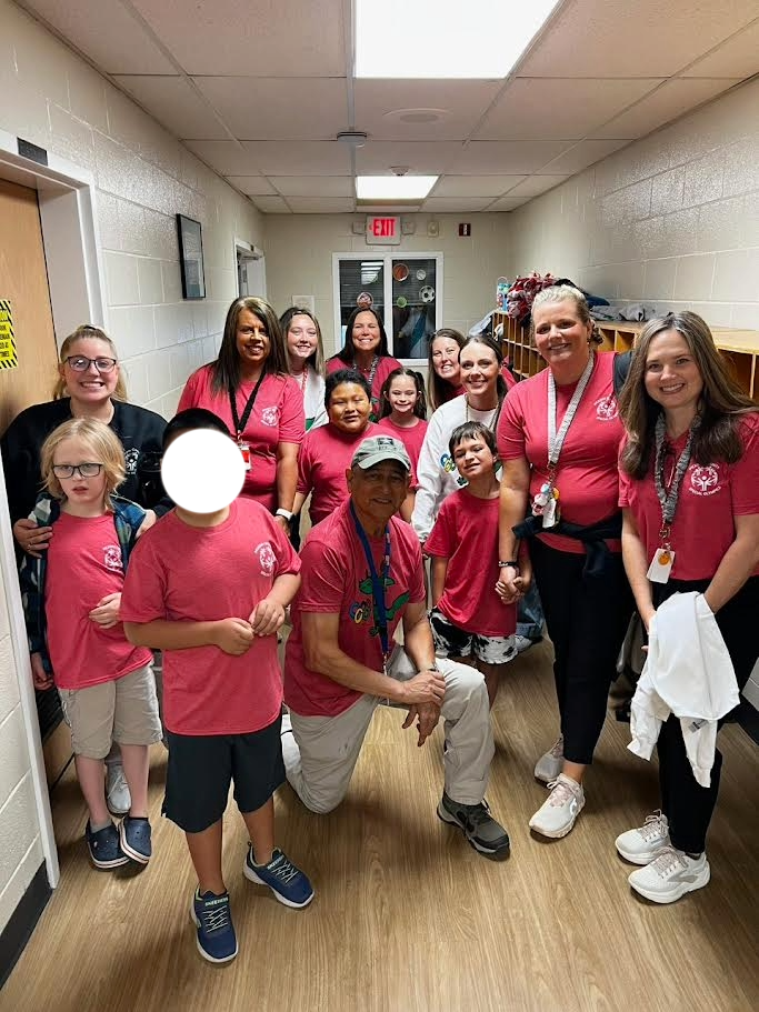 Students and staff wearing pink. Standing and some are kneeling in a school hallway.