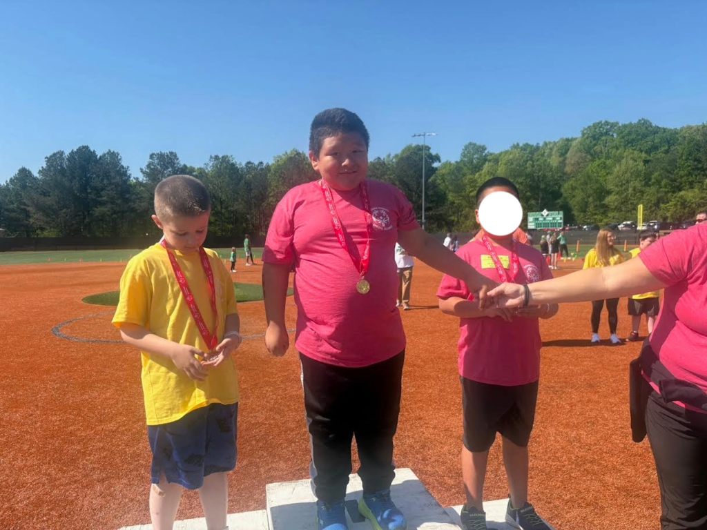 Three kids standing on a podium. Two are wearing oink, one is wearing yellow