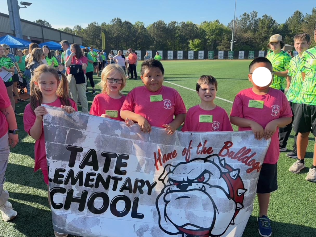 Kids in pink shirts holding a sign that says Tate Elementary School Home of the Bulldogs