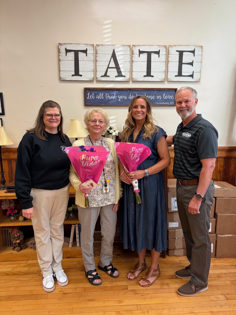 Four people standing, three women, one man. Two of the women standing in the middle are holding flowers