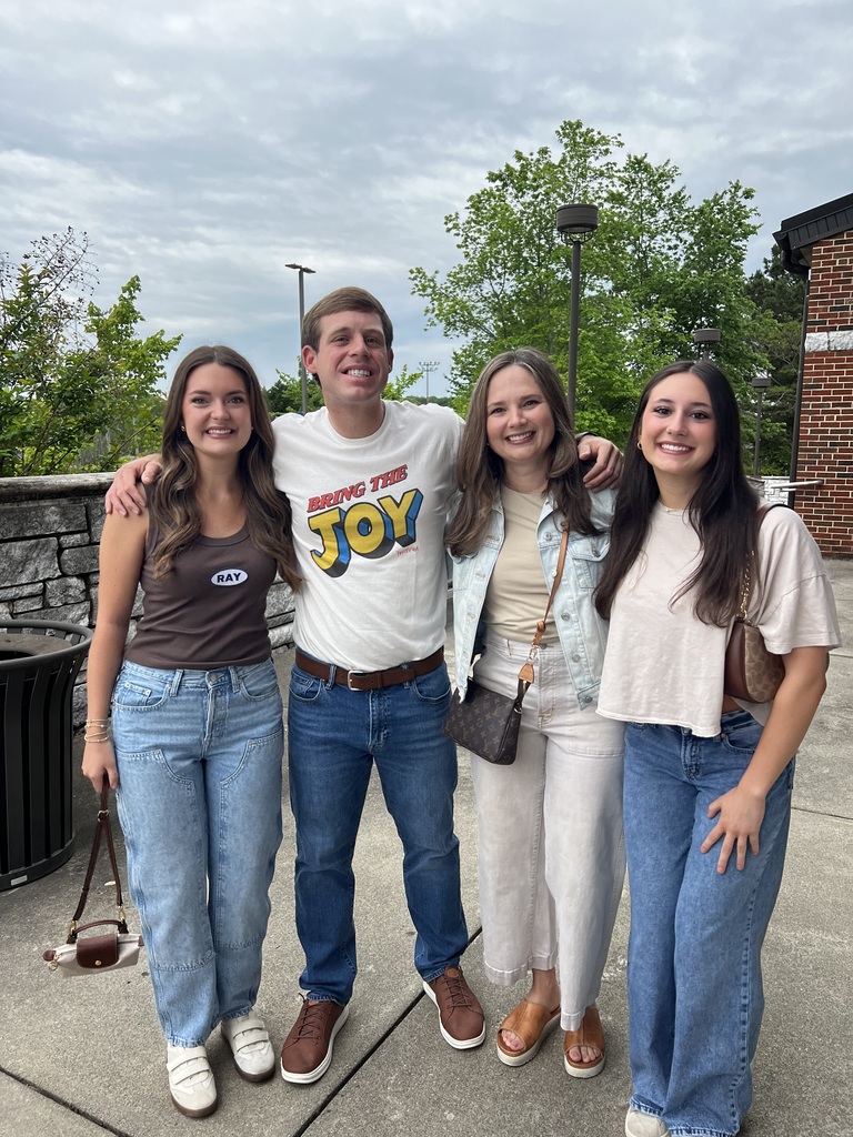 three women and one man standing close with their arms around each other. 