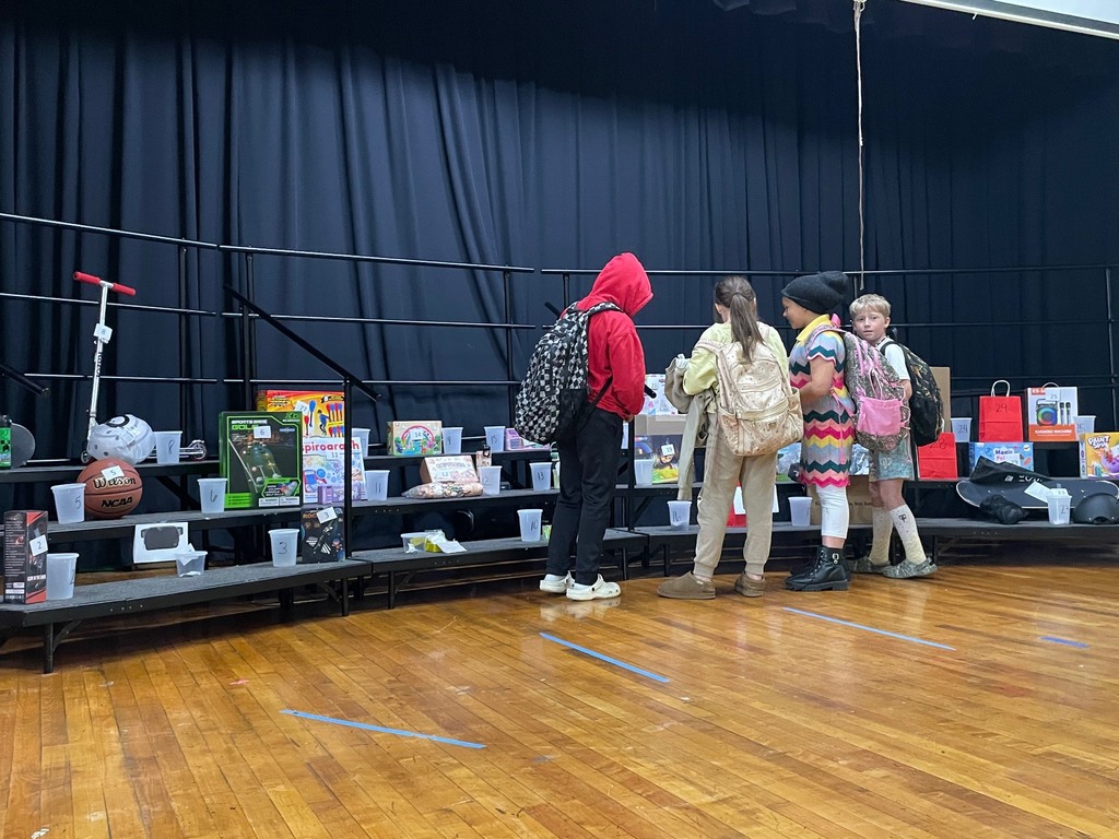 Four kids standing on a stage in front of a riser with prizes