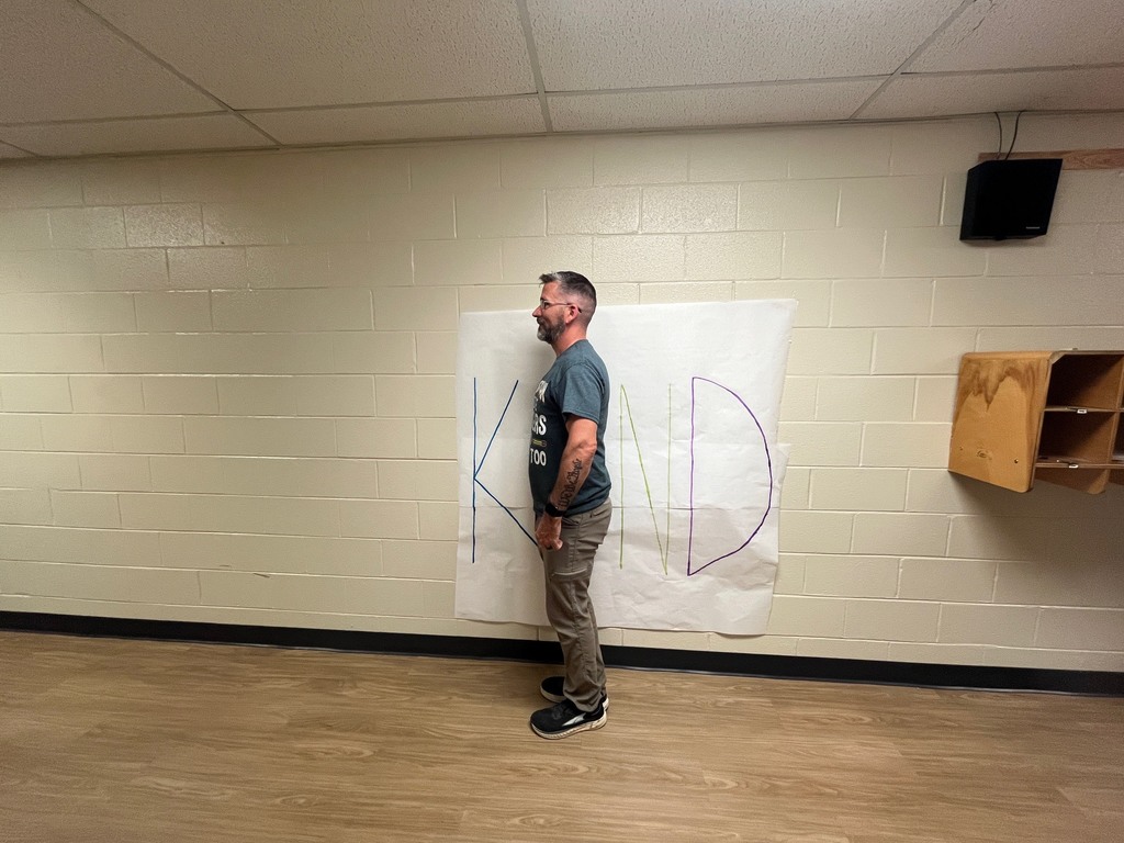 Man standing in front of a poster with the letters  K N D. His body is being used as the letter I