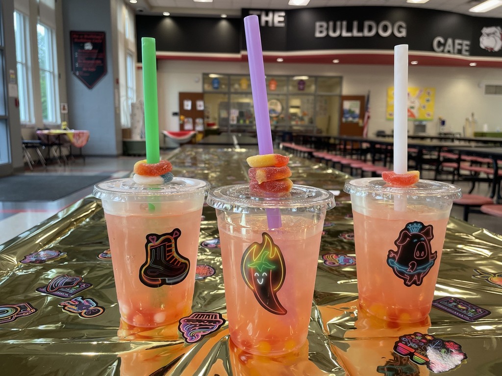 Three cups with stickers, a skateboard sticker a jalepeno sticker, and a pig wearing a tutu sticker. Liquid is in the cup. There are circle candy gummy rings around the straw.