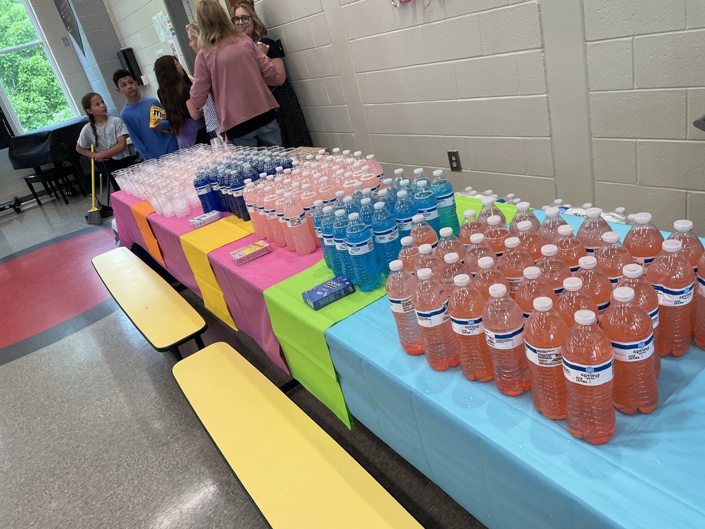 Table with colorful tablecloths. Clear plastic cups filled with ice , and bottled waters are sitting on the tables. 