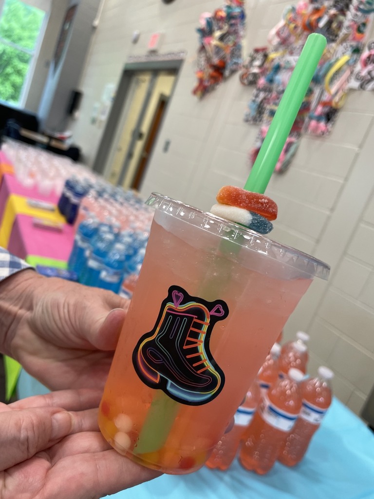  clear plastic cup with a  skateboard sticker. Liquid is in the cup. There are circle candy gummy rings around the straw.