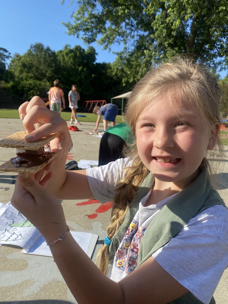 One female student holding a smore. Four kids are in the background not looking at the camera