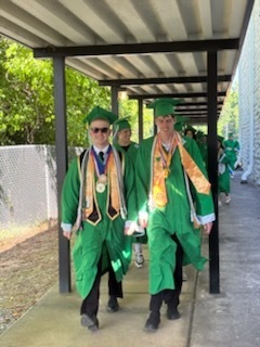Two male high school students wearing green graduation gowns 