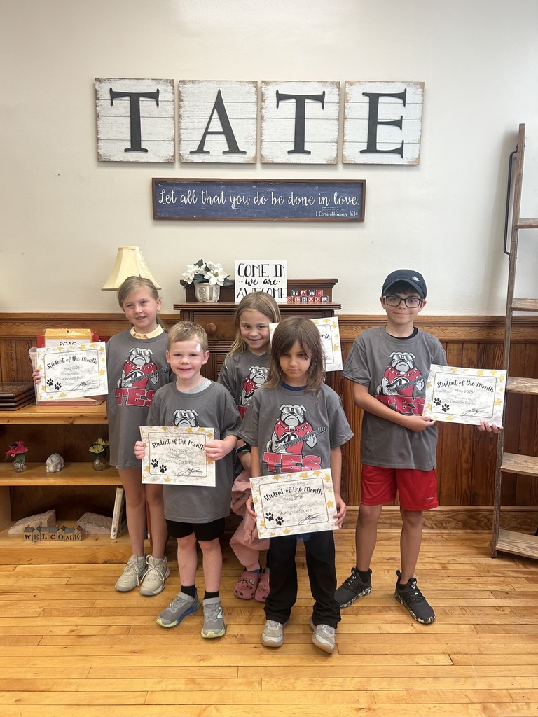Five kids standing together in front of a sigh that reads TATE. All of them are wearing the same shirt and holding certificates.