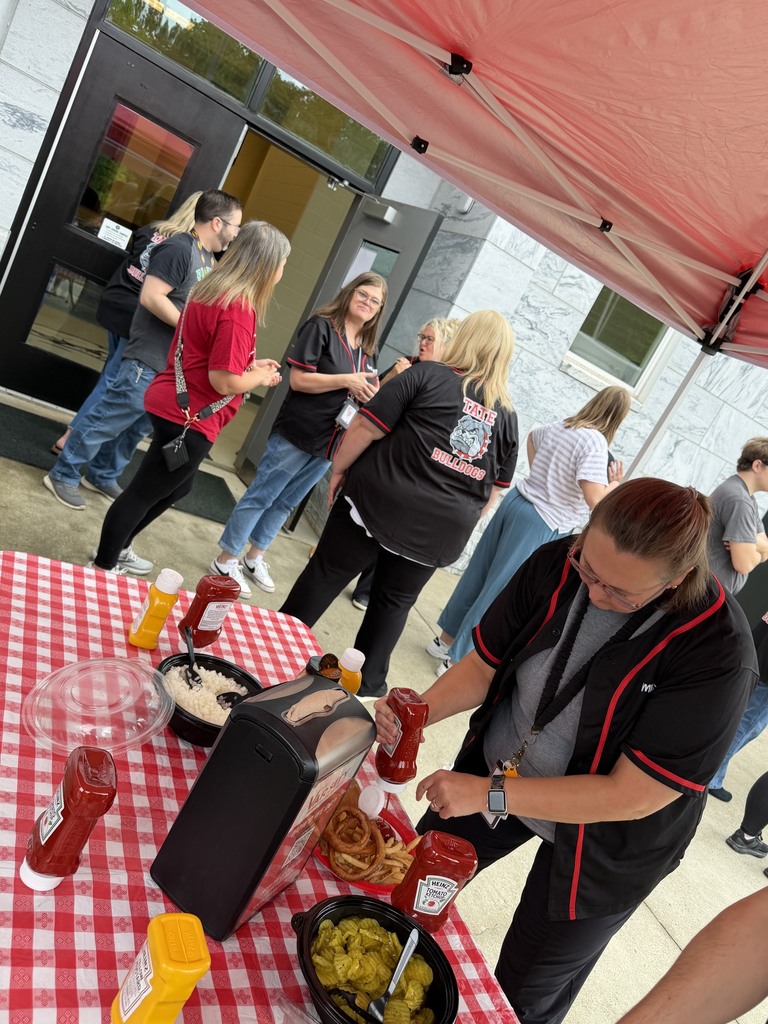 group of people standing around, some are under a tent making a plate of food, some are waiting in line