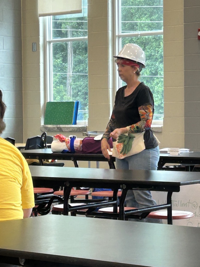  Woman with a white hard hat, black shirt, jeans, and arm tattoo sleeves standing in a school cafeteria