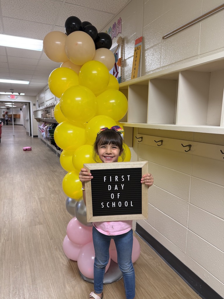 small female student holding a first day of school sign. Pencil balloon arch is in the background.