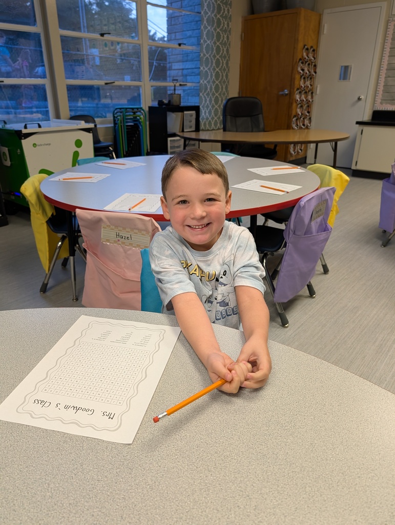 boy sitting at a table holding a pencil and smiling