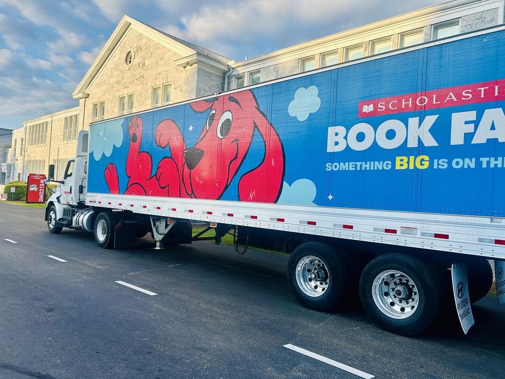 A large blue box truck trailer, featuring colorful graffiti and the text “SCHOLASTIC” and “BOOK FAIR,” with “SOMETHING BIG IS ON TH…” visible on the side.