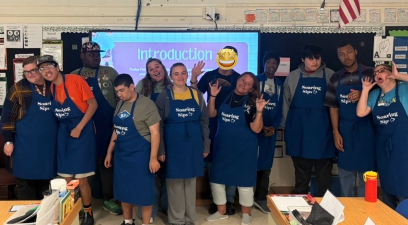Students in Palmer’s Pac wear Soaring Sips aprons and pose together playfully in the classroom, celebrating their student-run coffee shop at MKL.