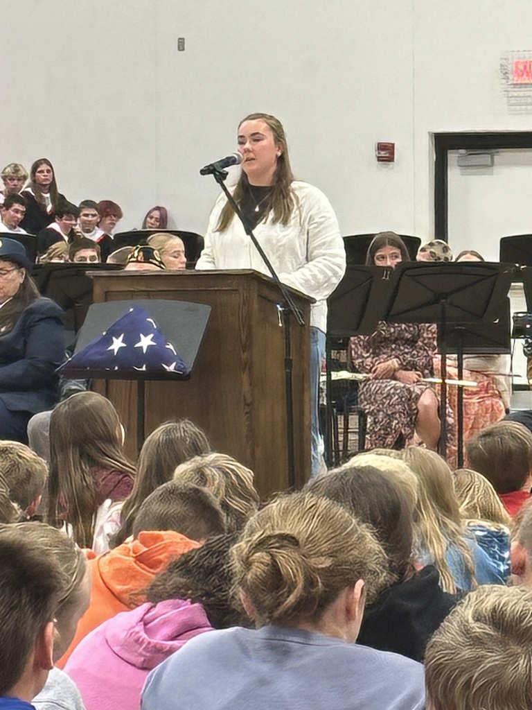 Lucy Caughy reading to students from behind a mic in Mac Gym