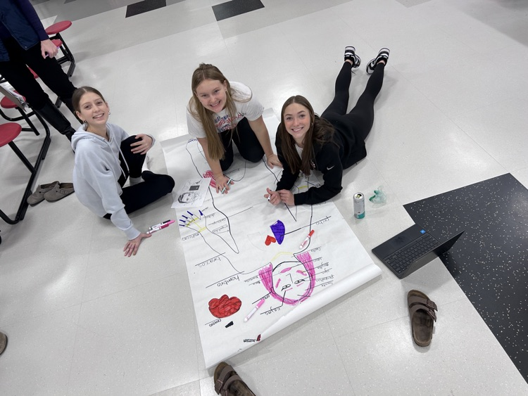3 students with art project on floor looking at camera 