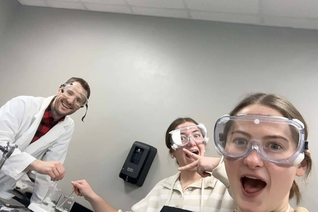students and teacher in chemistry goggles looking at camera